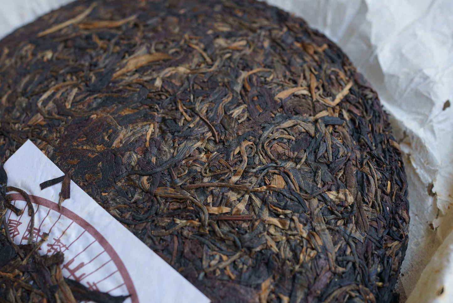 Close-up of vintage 2004 Shun Shi Xing Yiwu Ancient Tree raw Pu-erh tea cake — aged Sheng Pu-erh with visible tea buds and natural dry aging, highlighting rich leaf texture and authentic Yunnan mountain craftsmanship – Tea & Leaf