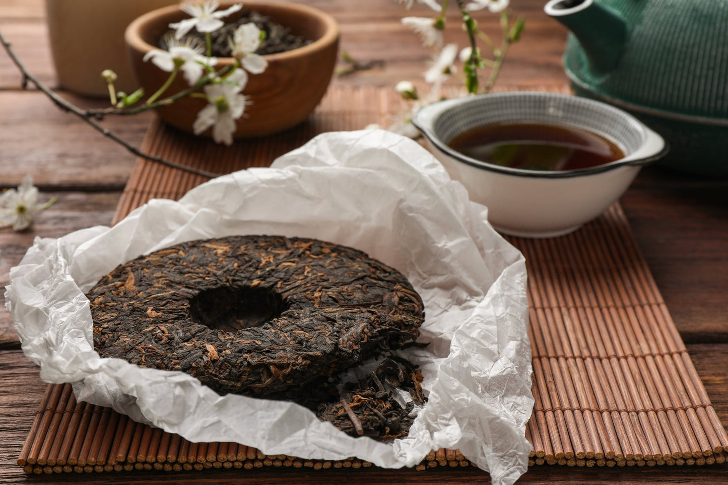 Compressed Pu-erh tea cake with brewed tea cup on bamboo mat — learning how to identify authentic Yunnan Pu-erh and taste its aroma, texture, and Cha Qi.