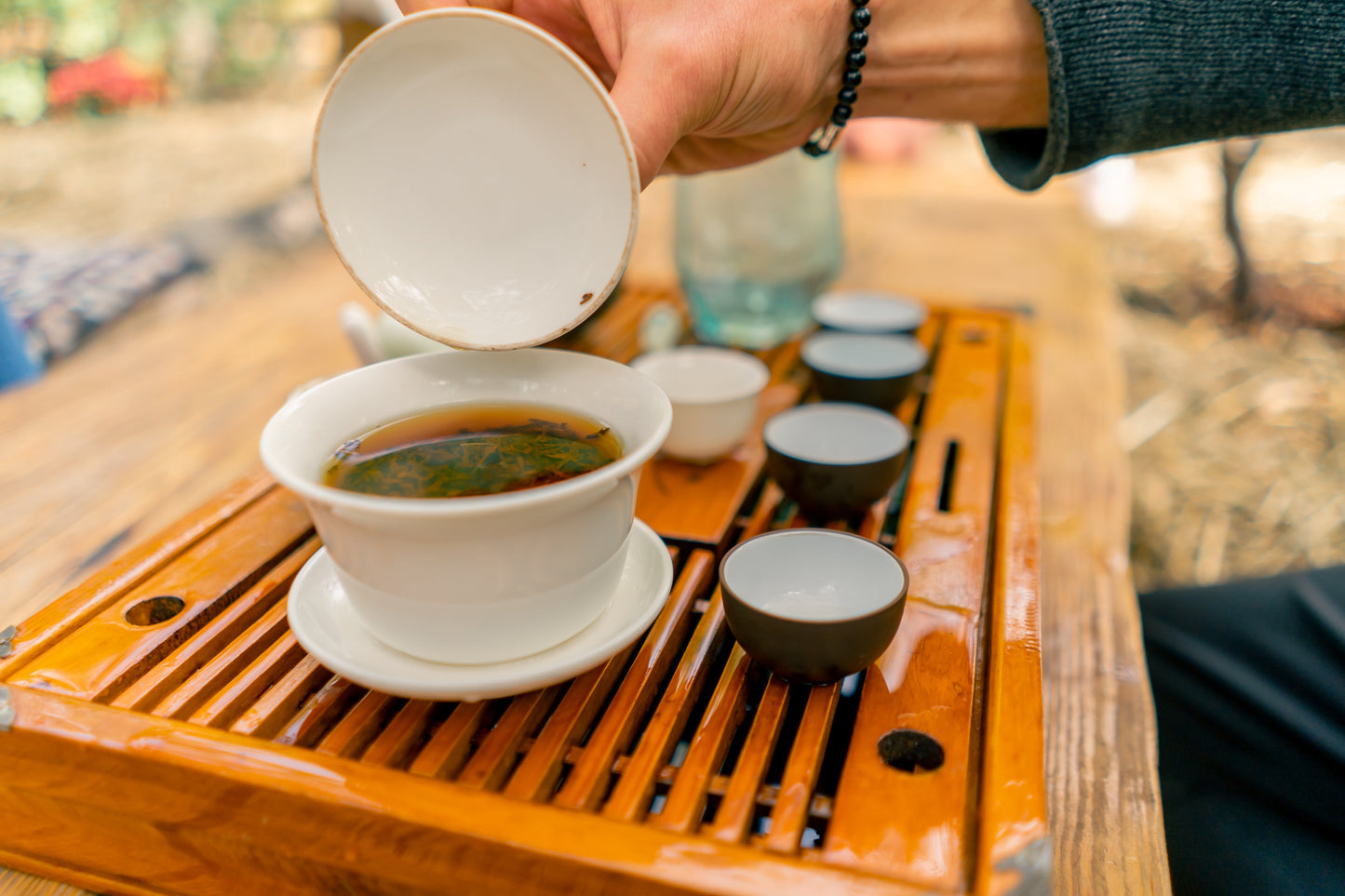 Traditional Gongfu tea ceremony with freshly brewed Pu-erh tea in a white gaiwan on a wooden tea tray, showcasing Yunnan’s ancient Chinese tea culture and brewing tradition.