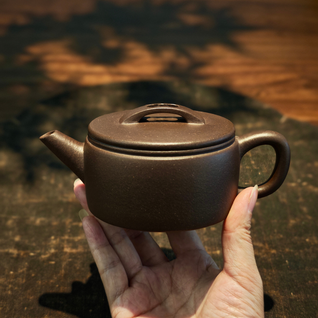 Handcrafted Yixing Zisha Han Wa Tai Xi teapot made from Zi Ni purple clay, 160ml Gongfu teapot held in hand — traditional Chinese teaware from Yixing for Pu-erh, oolong, and black tea brewing in an elegant tea ceremony setting.