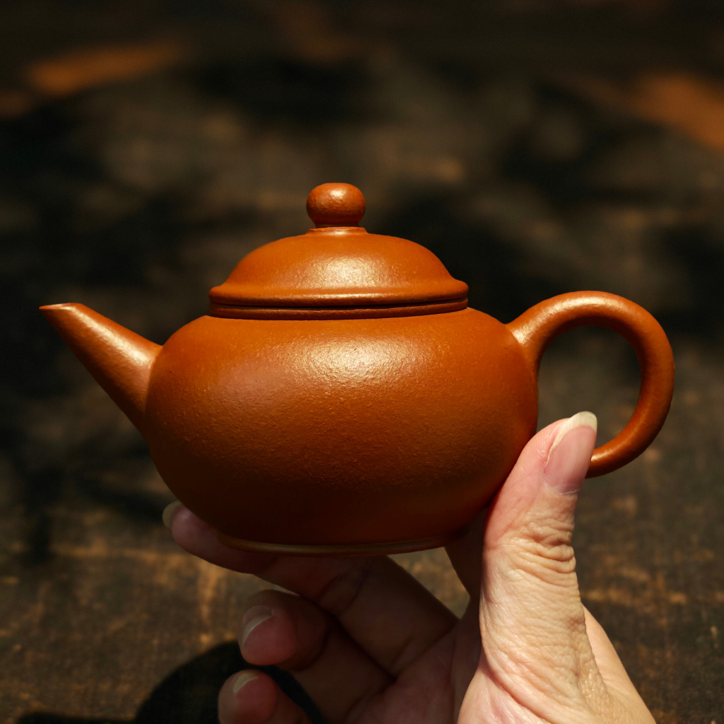 Handcrafted Yixing Zisha Shui Ping teapot made from Lao Hongni red clay, 160ml Gongfu teapot shown being held in hand under warm light — traditional Chinese teaware designed for brewing Pu-erh, oolong, and black teas.