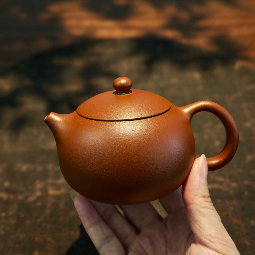 Handcrafted Yixing Zisha Xi Shi teapot made from authentic Lao Hongni red clay, 160ml Gongfu tea teapot shown in hand under warm lighting, ideal for Pu-erh and oolong tea brewing.