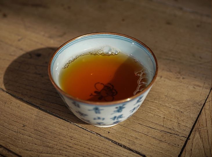Golden amber liquor of vintage 1995 private customized 8582 recipe Bulang Ancient Tree raw Pu-erh tea — aged Sheng Pu-erh brewed to perfection in porcelain cup, showcasing rich color and clarity – Tea & Leaf.