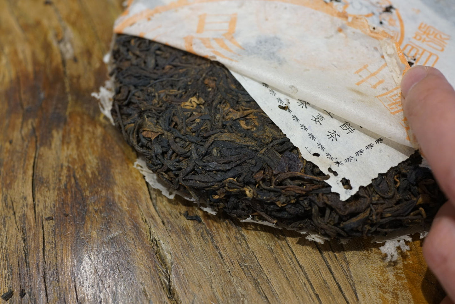 Unwrapping 1999 Yichang Hao Songti vintage raw Pu-erh tea cake, showing aged Sheng Pu-erh leaves and traditional orange Chinese label on wooden table – Tea & Leaf.