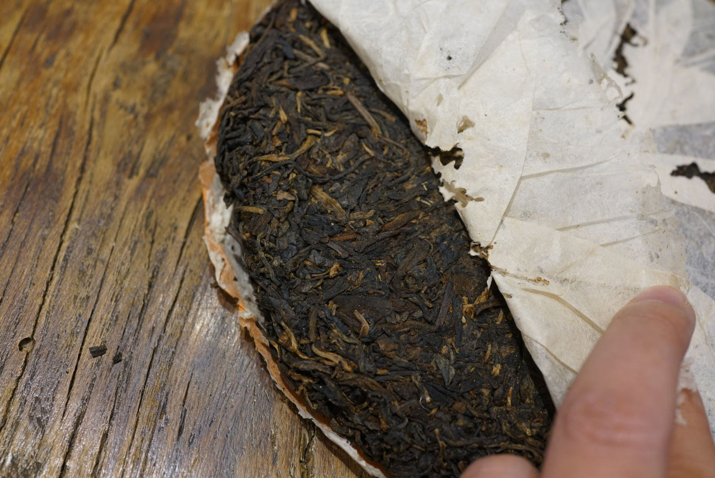 1999 Yichang Hao Songti vintage raw Pu-erh tea cake being unwrapped, showing aged Sheng Pu-erh leaves with dry storage patina on wooden table – Tea & Leaf.