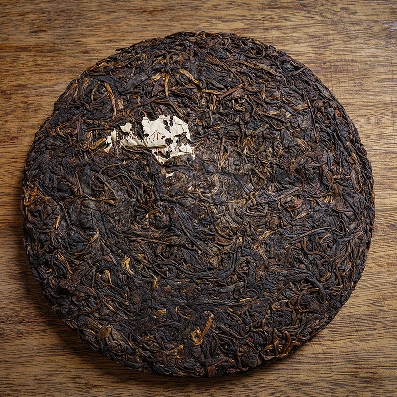 Vintage 2002 Huisheng Hao Yiwu Old Tea Garden Ancient Tree raw Pu-erh tea cake — aged Sheng Pu-erh 357g showing dark, tightly compressed tea leaves with golden tips and natural dry aging on wooden surface – Tea & Leaf.