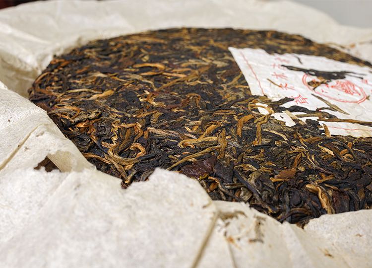Close-up side view of vintage 2004 Liming Tea Factory Ban Zhang Ancient Tree raw Pu-erh tea cake — aged Sheng Pu-erh showing golden tea buds, rich leaf compression, and original red label – Tea & Leaf.
