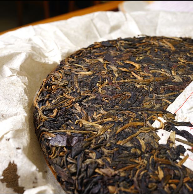 Side view of vintage 2004 Liming Tea Factory Ban Zhang Ancient Tree raw Pu-erh tea cake — aged Sheng Pu-erh with golden buds and rich leaf texture on handmade paper wrapping – Tea & Leaf.