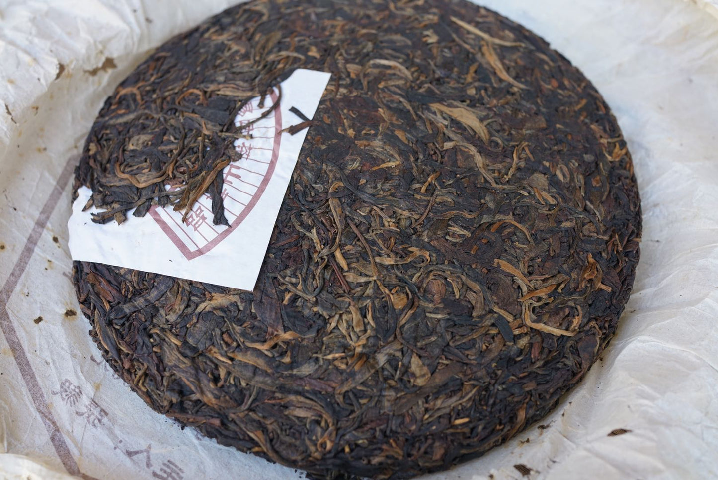 Unwrapped vintage 2004 Shun Shi Xing Yiwu Ancient Tree raw Pu-erh tea cake — aged Sheng Pu-erh with visible tea buds and natural dry-aged compression, showcasing authentic Yunnan craftsmanship – Tea & Leaf.