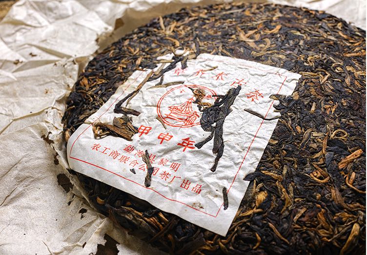 Close-up of vintage 2004 Liming Tea Factory Ban Zhang Ancient Tree raw Pu-erh tea cake — aged Sheng Pu-erh showing golden tea buds and red factory label on handmade paper – Tea & Leaf.